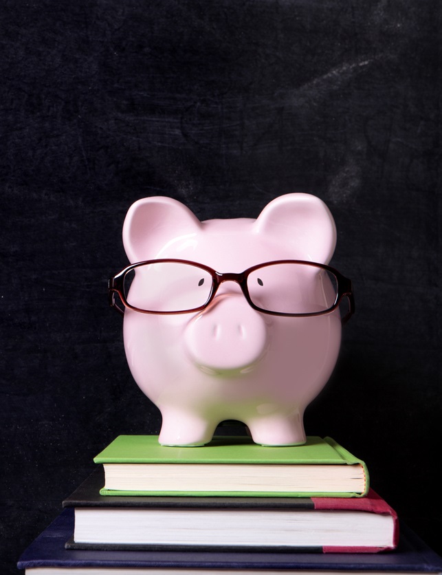 Piggy Bank with Glasses on Stack of Books Behind Blackboard