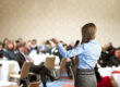 Young woman speaks to tabled audience at business conference