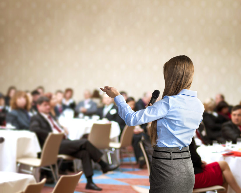 Business conference Young woman speaks to tabled audience at business conference