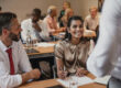 Group of business people sit at desks and face speaker in small conference room