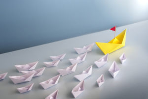 Paper boats being led by a leader boat origami