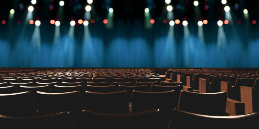 empty vintage seat in auditorium or theater with lights on stage.