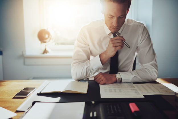 Serious business man working on documents Optio Solutions Man Studying
